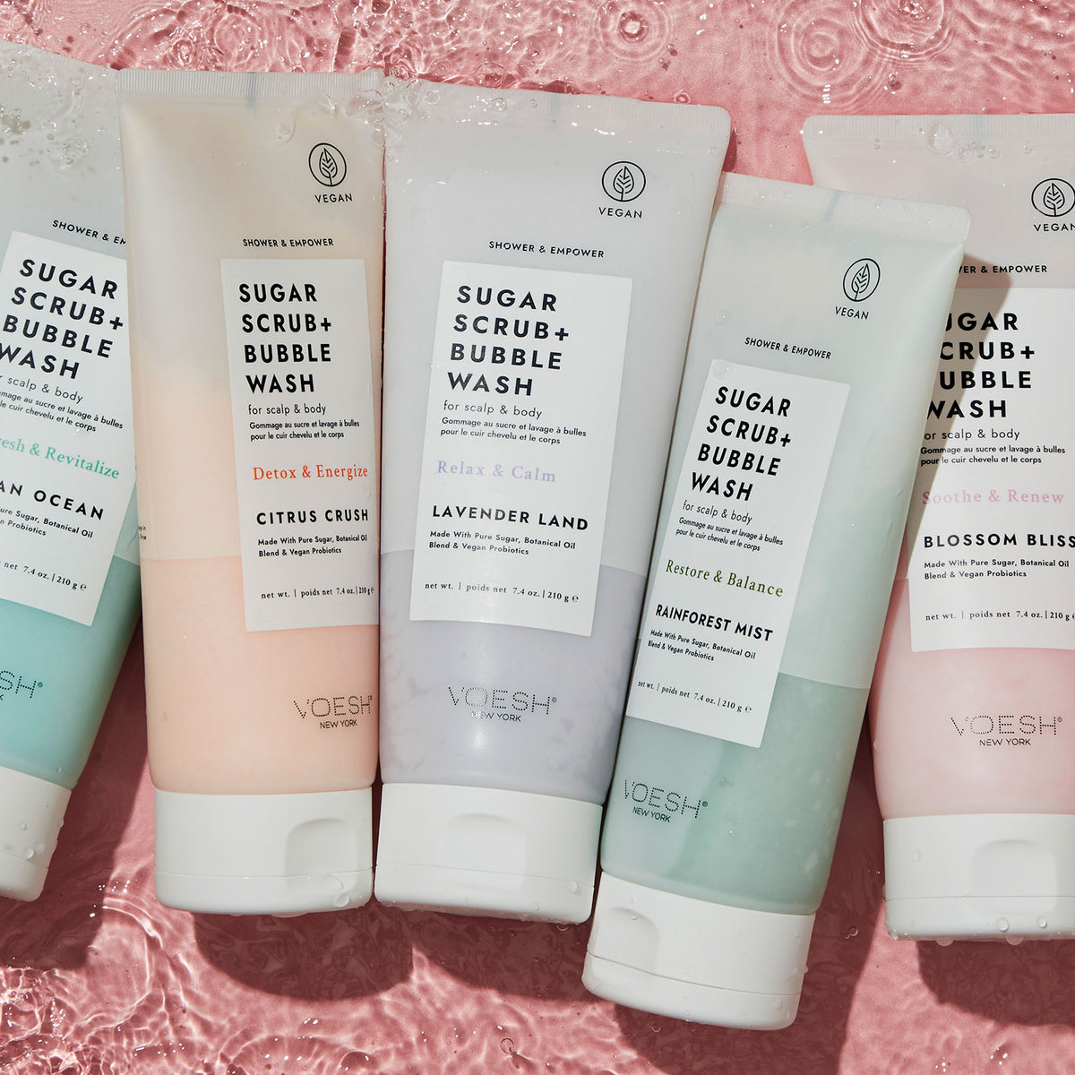 A variety of VOESH Sugar Scrub and Bubble Wash tubes being held by a woman in a white bath robe