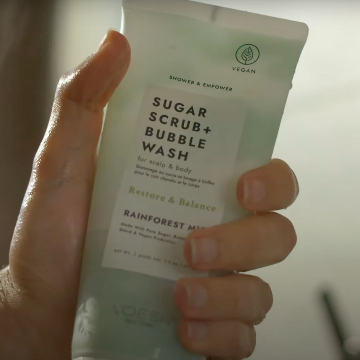 A mans hand holing Voesh's Sugar Scrub and Bubble Wash in Rainforest Mist