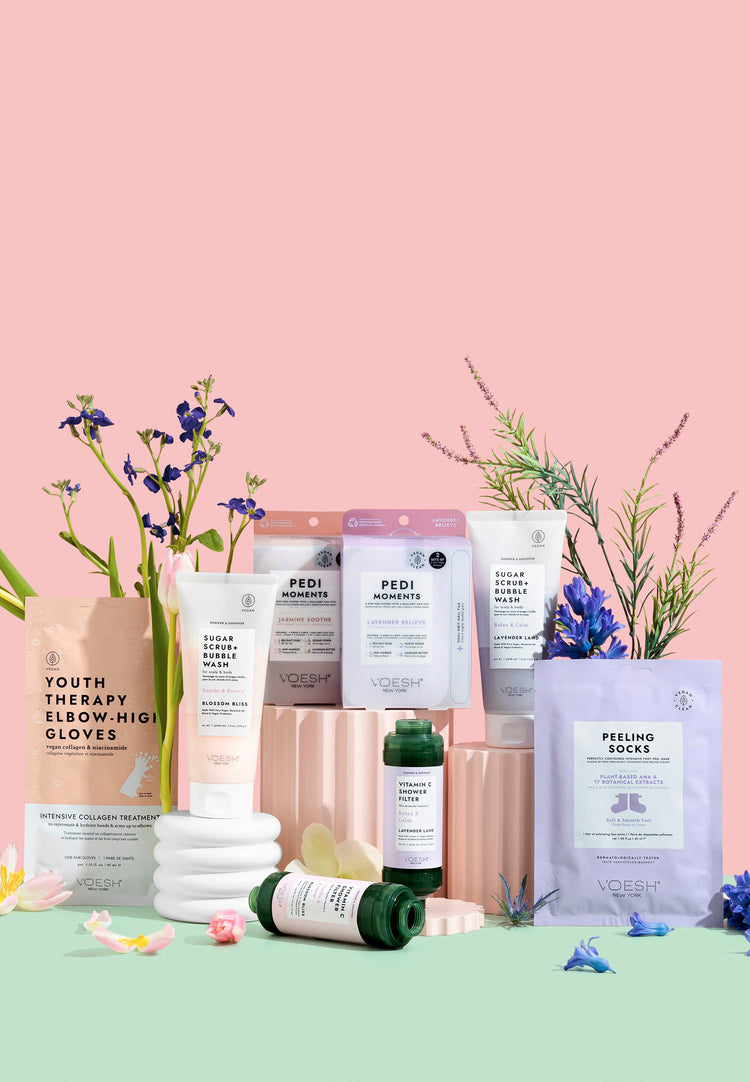 Variety of VOESH body care products on a pink background with purple flowers.
