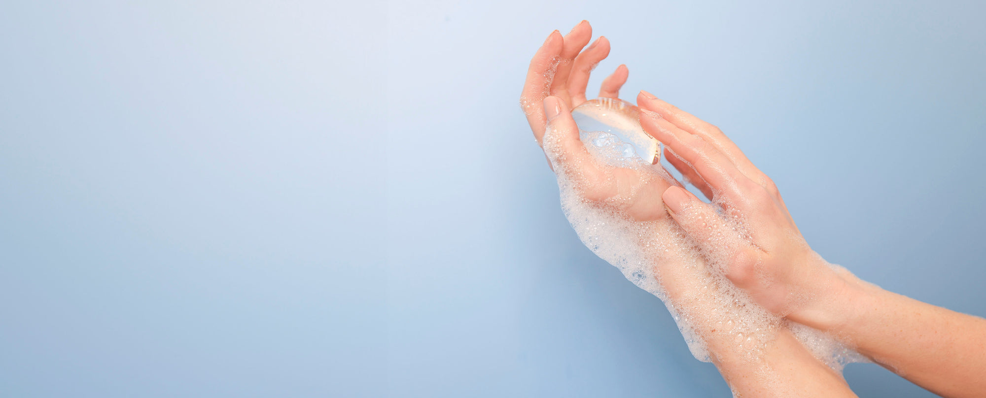 Woman’s hands lathering up Crystal Clear Head-To-Toe Cleansing Soap pictured on a blue background.