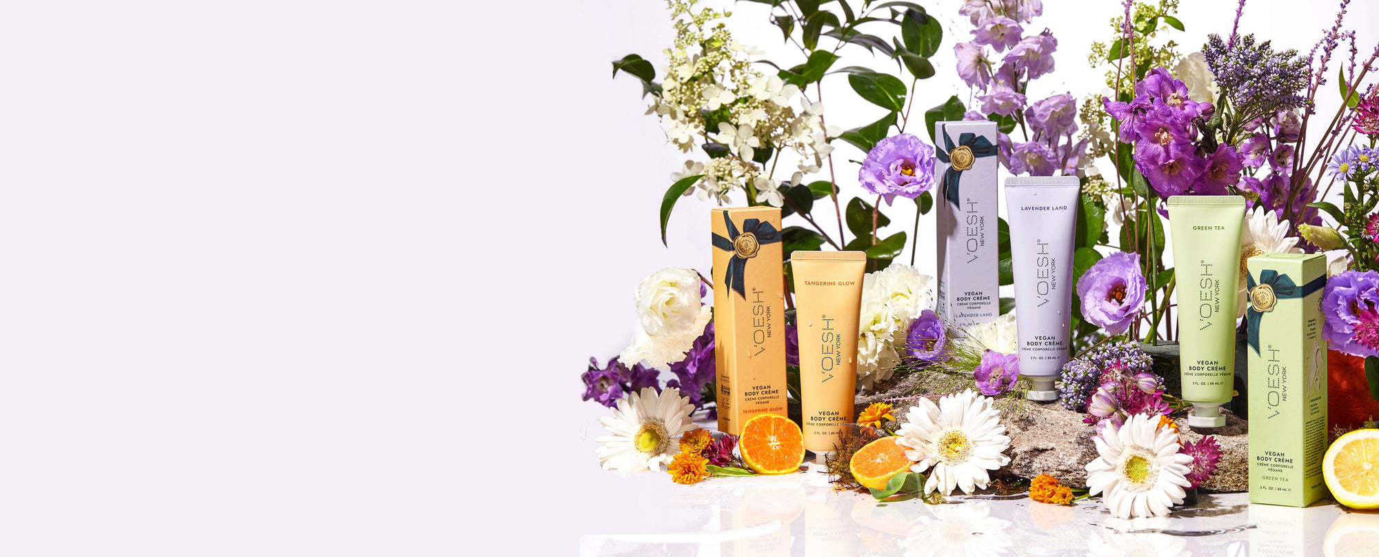 Vegan Body Crème Trio on a light purple background with colorful flowers and orange and lemon slices.