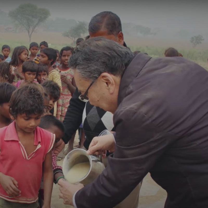 Man with back turned to camera pouring out food for child with group of children behind him