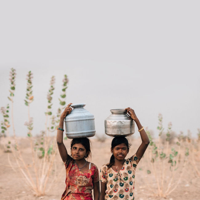 Two young girls on the plains carrying water jugs on their heads