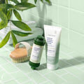 Rainforest Mist Shower & Empower Duo with a dry body brush, white towel, and plants on a green tiled background.