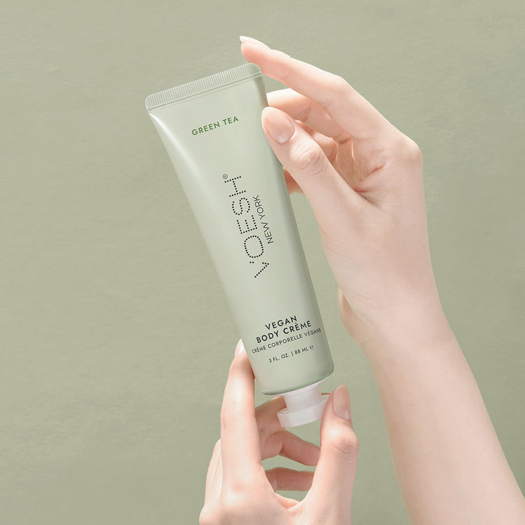 Woman’s hands holding Green Tea Vegan Body Crème on a green background.