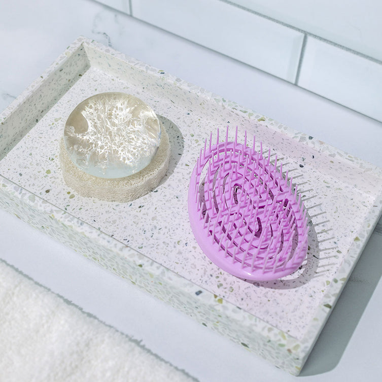 Crystal Clear Head-To-Toe Cleansing Soap on top of the Natural Loofah Soap Dish and next to the Scalp Massager, pictured on a vanity tray with a white subway tile background.