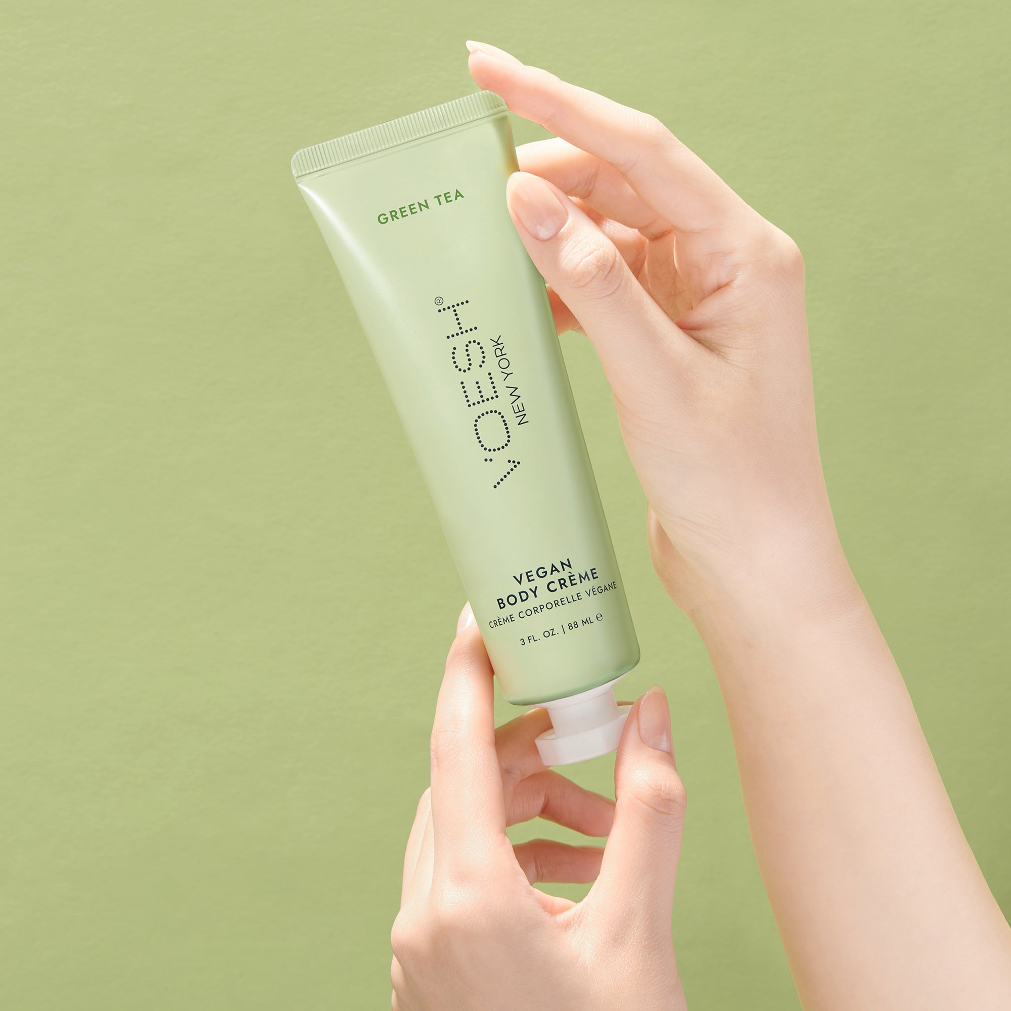 Woman’s hands holding Vegan Body Crème Green Tea on a green background.