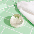 Crystal Clear Head-To-Toe Cleansing Soap on top of the Natural Loofah Soap Dish next to a white towel on top of green subway tile.