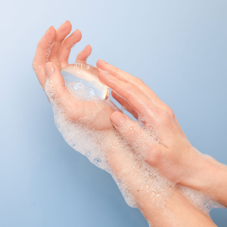 Woman’s hands holding Crystal Clear Head-To-Toe Cleansing Soap in a soapy lather on a blue background.