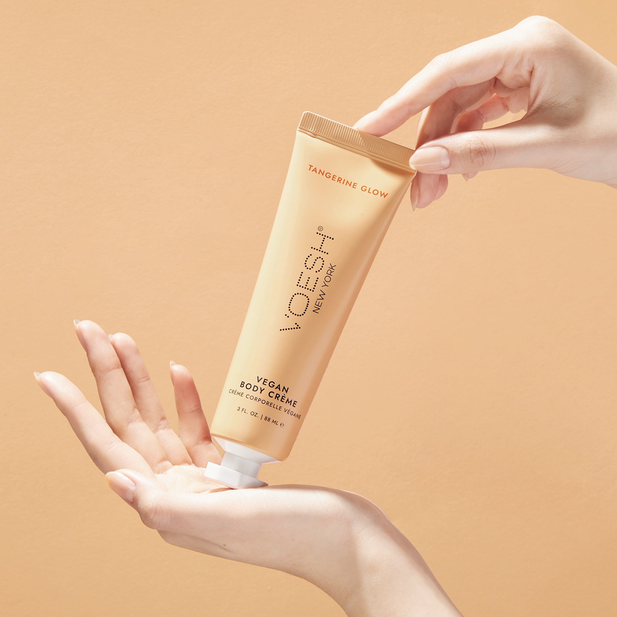 Woman’s hands holding Vegan Body Crème Tangerine Glow on an orange background.