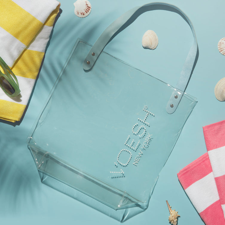 Clear Beach Bag on a blue background with seashells, beach towels, and sunglasses.