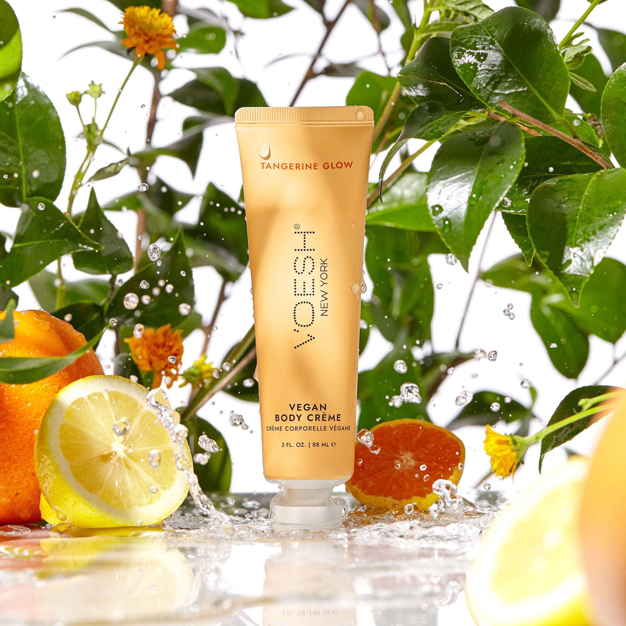 Vegan Body Crème Tangerine Glow in front of orange flowers, green leaves, lemon, and orange slices.