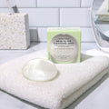 Crystal Clear Head-To-Toe Cleansing Soap on a white towel on a bathroom vanity with a white subway tile background.