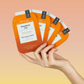 Hands holding Pumpkin Pie Pedi In a Box 4 Step Packets on orange and yellow gradient background