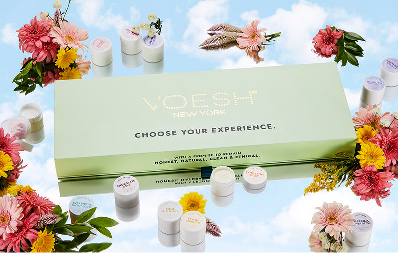voesh scent box with scent balms surrounding it on a cloud background and pink and yellow flowers