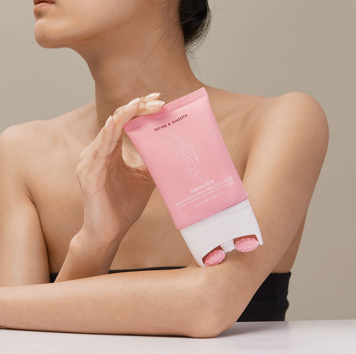 Woman holding Smooth’d Body Refining Roller Crème and leaning it on her forearm, pictured on a tan background.Woman holding Smooth’d Body Refining Roller Crème and leaning it on her forearm, pictured on a tan background.