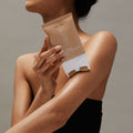 Woman holding Tone’d Body Firming Roller Crème on her upper arm, pictured on a gray background.