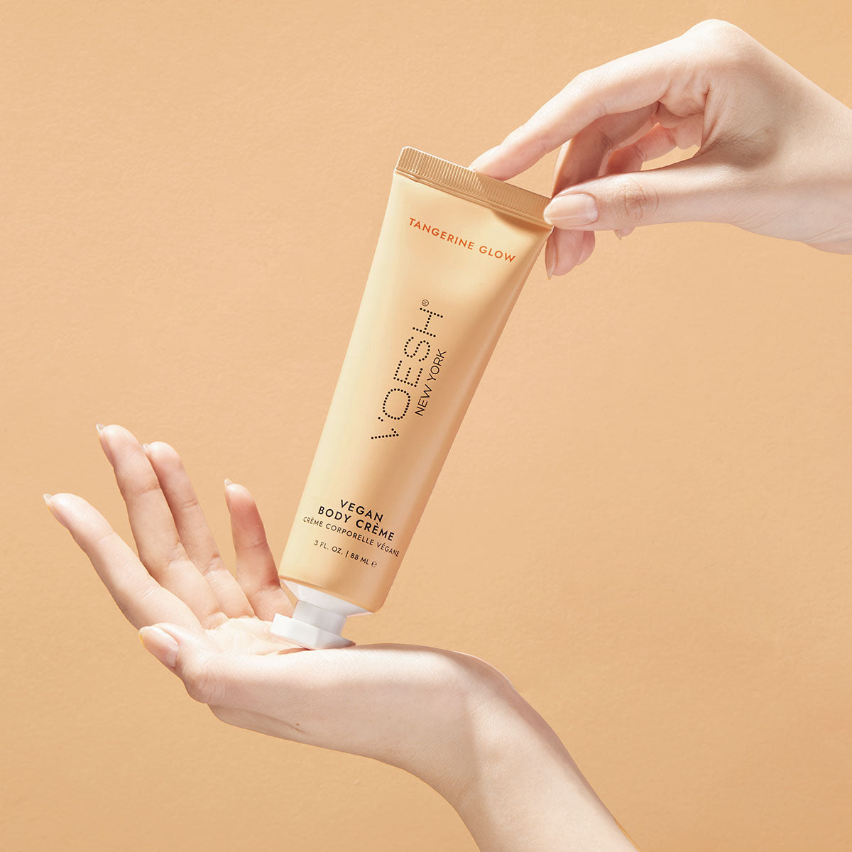 Woman’s hands holding Tangerine Glow Vegan Body Crème on an orange background.