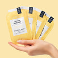 woman's hand holding lemon quench pedi in a box 4 step packets on yellow background