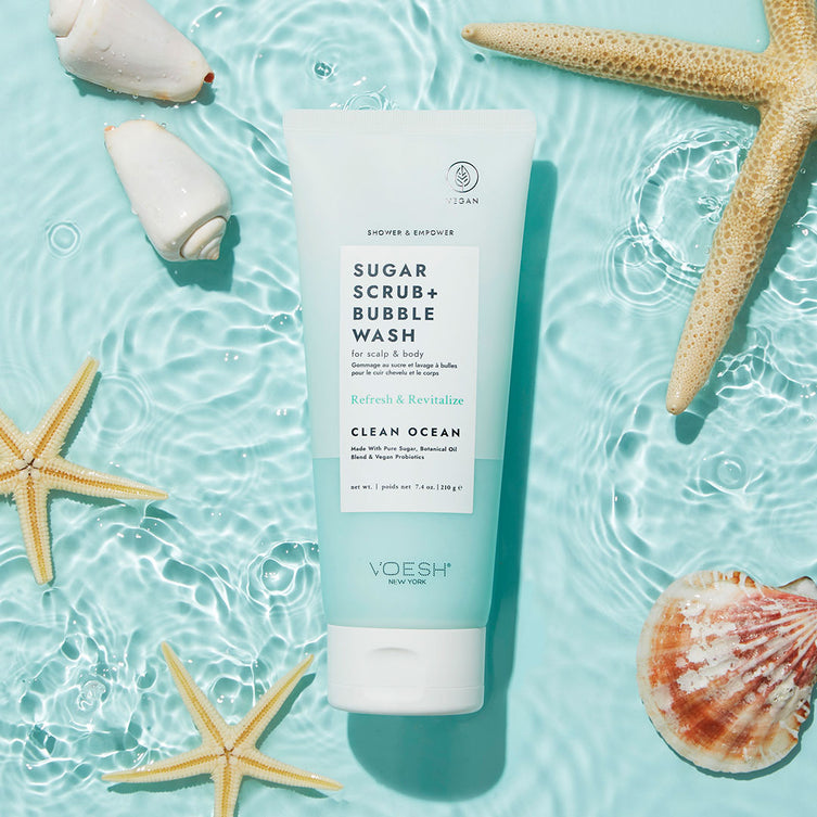 Clean Ocean Sugar Scrub + Bubble Wash in water with sea shells surrounding on blue background