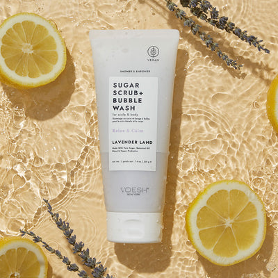 Lavender Land Sugar Scrub + Bubble Wash on yellow background with lemon slices and lavender branches in water